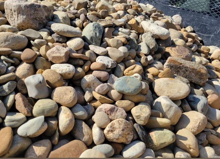 A large pile of smooth river rock in beige, grey and tan on the yard