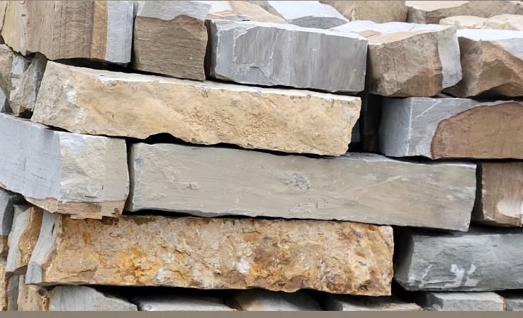 A stack of rough-hewn rectangular stone blocks in grey, beige and tan