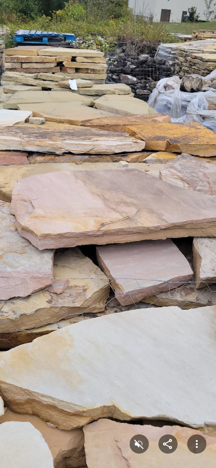 A tall stack of flat irregular flagstone slabs in pink, tan and cream at the stone yard