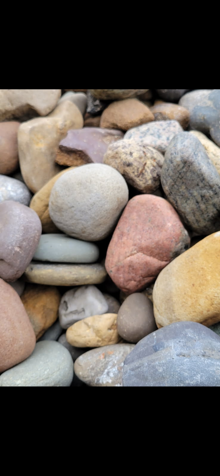 A tightly packed pile of smooth river stones in grey, tan, pink and reddish brown