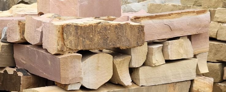 Rough-hewn sandstone blocks stacked in pink, tan and grey at the stone yard