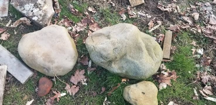 Two large weathered boulders resting whole on grass among fallen leaves